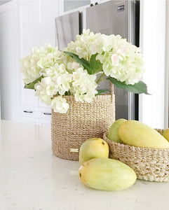 Sustainable handwoven home furnishings catch all tray bucket with white flowers mangoes in a bowl in white modern kitchen