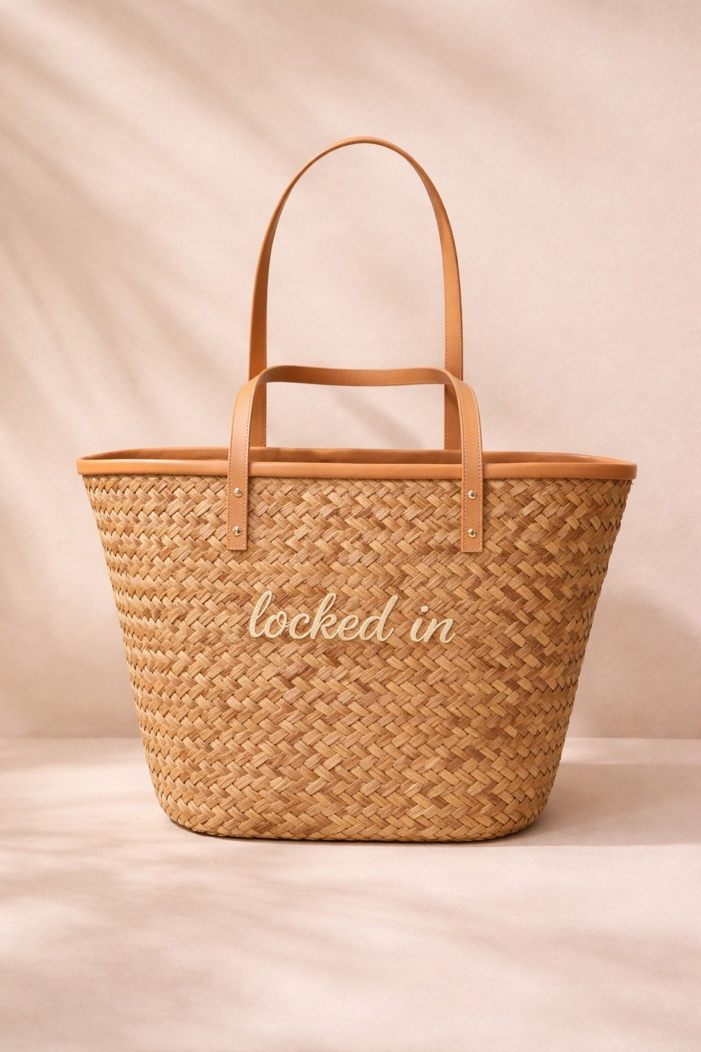 Woven bag with leather handles and 'locked in' text on a beige background