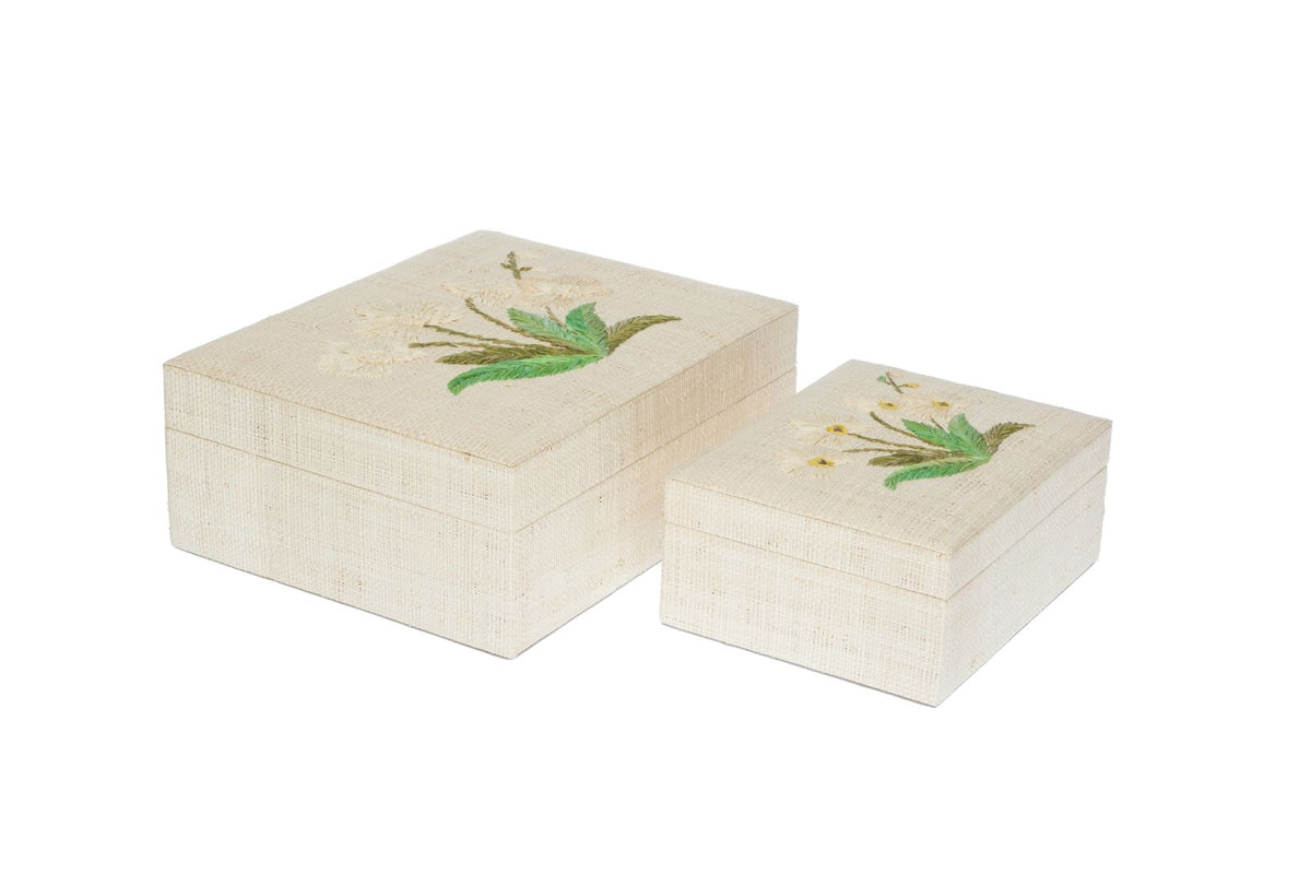 Two rectangular cream-colored woven fabric storage boxes with matching lids, decorated with green and gold floral designs on the top, shown against a plain white background.