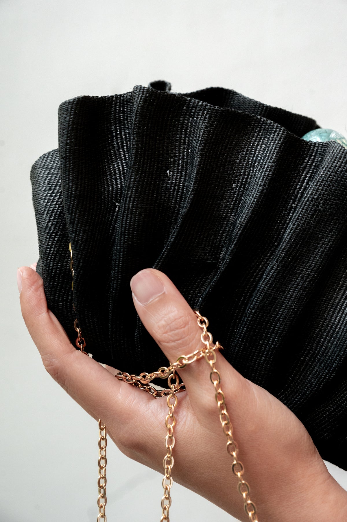 Close-up shot of a hand holding the Josephine Clamshell Clutch Black with the fine gold link chain draped across the fingers.