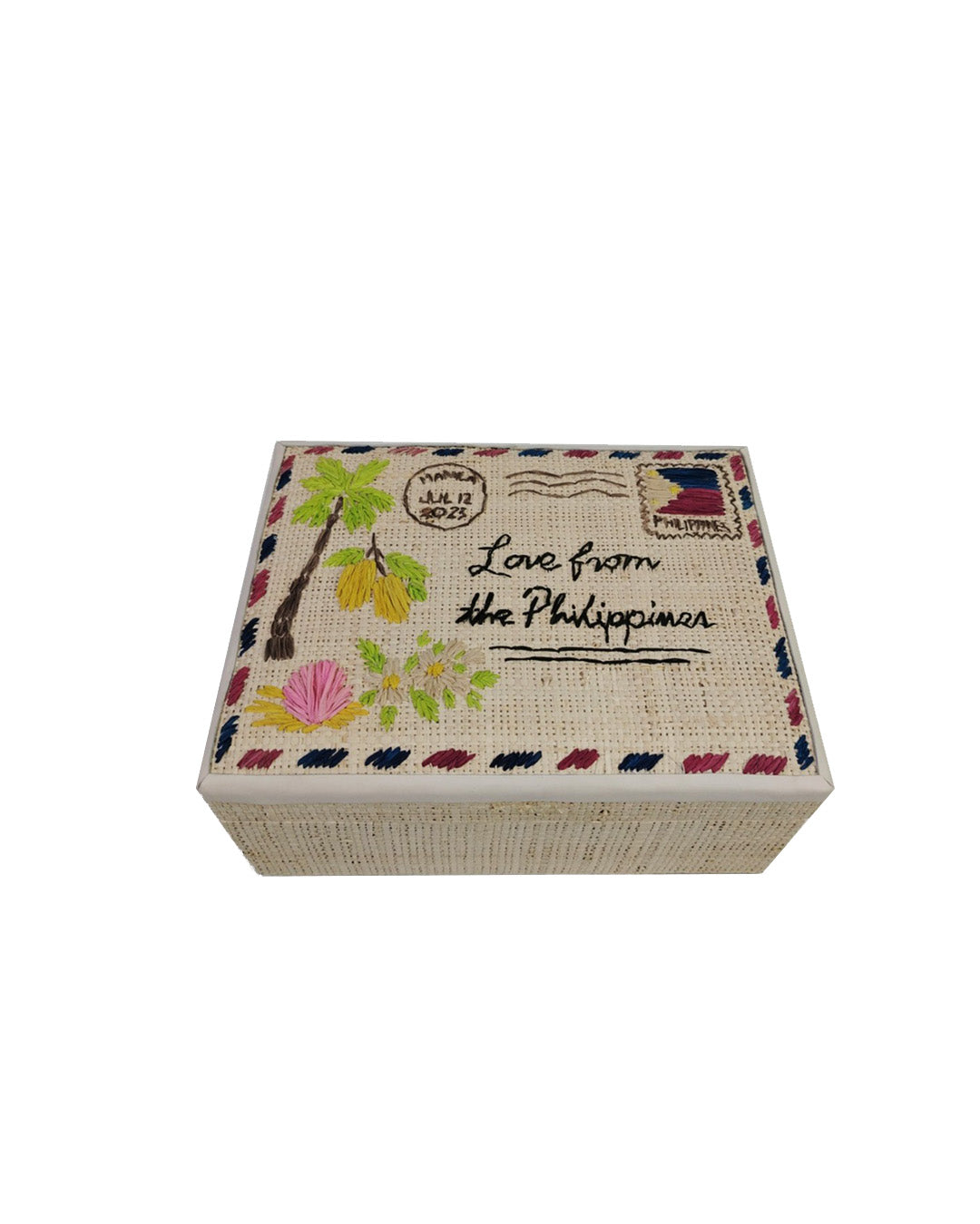 Top-down perspective of a woven raffia storage box with embroidered airmail postcard details reading Love from the Philippines.