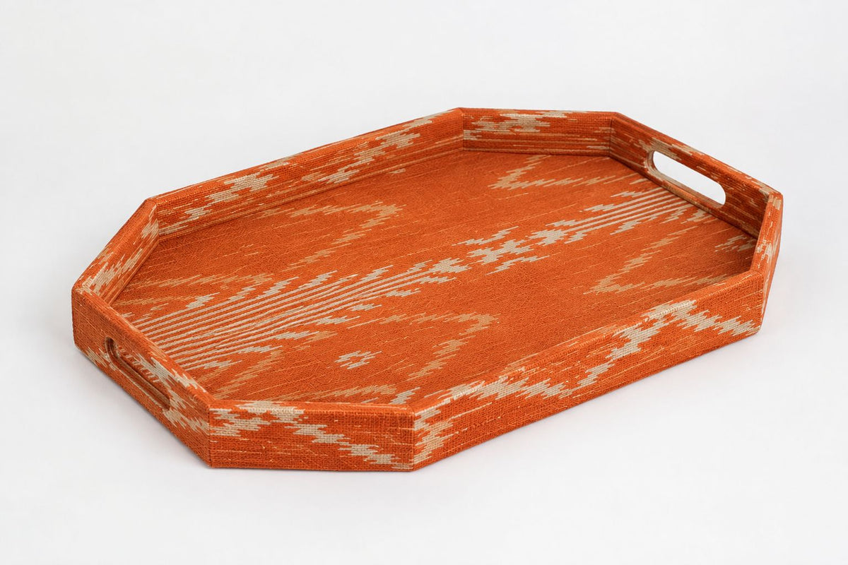 An octagonal woven tray with a vibrant orange and cream ikat pattern, featuring integrated side handles, shown on a plain white background.