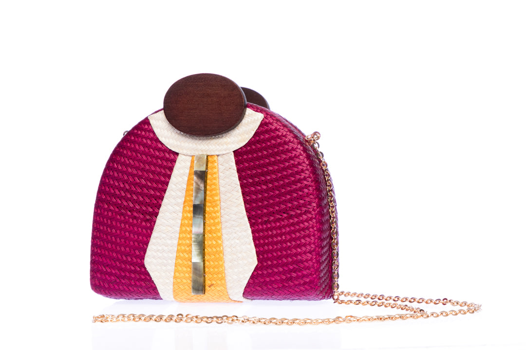 Gatsby Raspberry half-moon clutch made from handwoven natural plant fibers with a cracked sea shell bar and a brass chain strap, adding glamour and sophistication for any evening event.