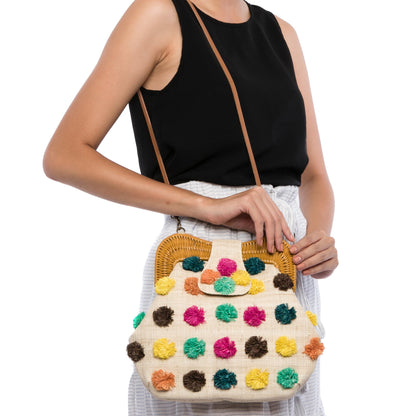 Forest Pompom Libby shoulder bag with handwoven raffia body, rattan frame, and fluffy raffia pompoms. Stylish and fun statement bag with leather strap.
