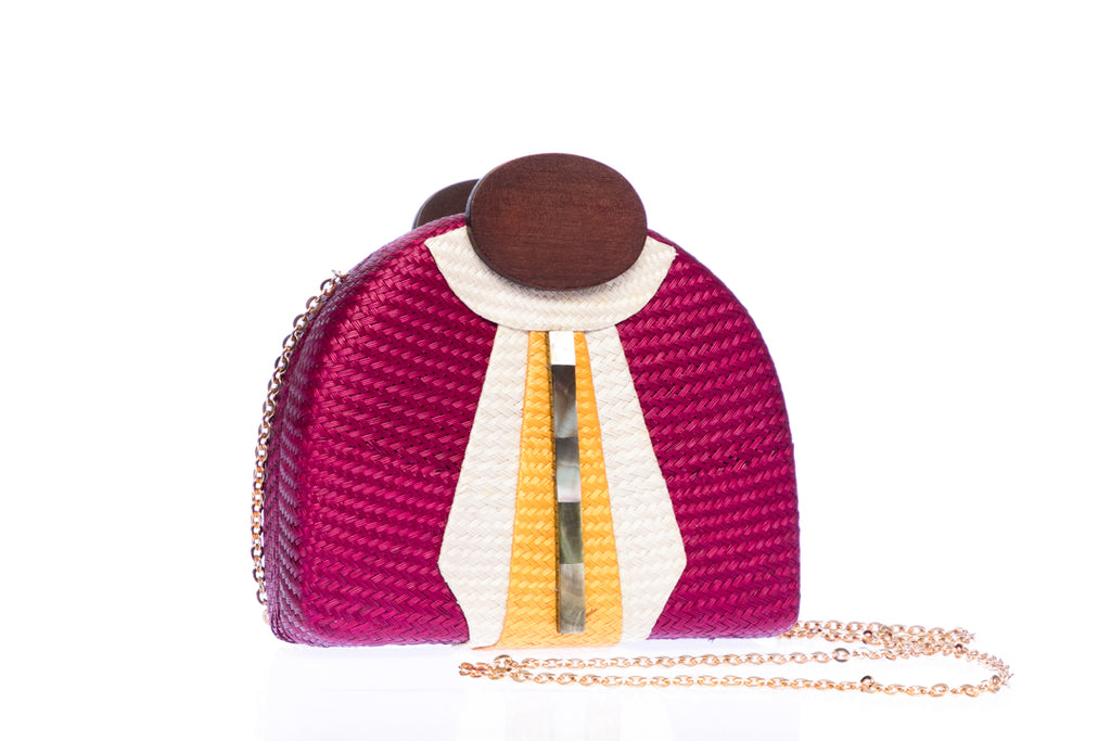 Gatsby Raspberry half-moon clutch made from handwoven natural plant fibers with a cracked sea shell bar and a brass chain strap, adding glamour and sophistication for any evening event.
